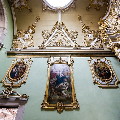 Museu da Misericórdia - Imagem de uma parede lateral da igreja de fundo verde claro, com três quadros grandes e teto em dourado